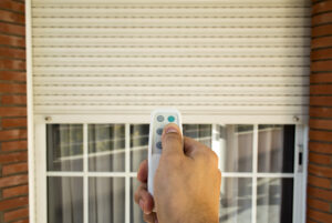 hand pressing a remote control with an electric roller shutter for home security